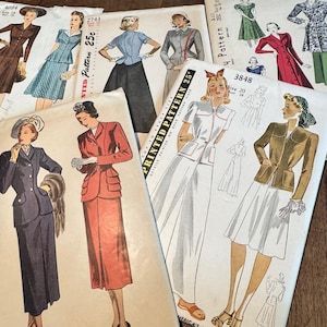May include: A collection of vintage paper sewing patterns featuring illustrations of various skirt and jacket ensembles. Each envelope displays printed text including pattern numbers 4034, 2743, 3848, and the brand name Simplicity, with illustrations of figures wearing coordinated outfits.