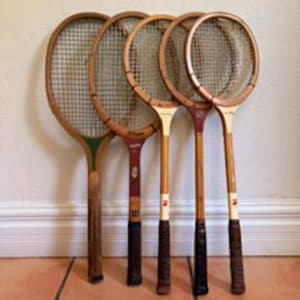 May include: A collection of five vintage wooden tennis rackets arranged in a row. Each racket features a wooden frame, a woven string bed, and a wrapped handle. The rackets display varying wood tones, colored accents, and branding logos on the shafts.