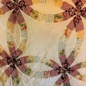 May include: Close-up of a handmade quilt featuring a Double Wedding Ring pattern. The quilt showcases interlocking rings and floral and striped fabric patches in shades of red, yellow, and green against a white background.