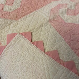 May include: A quilted textile featuring a white base with a diamond-stitched pattern and pink fabric accents. The design includes pink triangular fabric pieces attached along the edge, creating a decorative border against the white quilted surface.