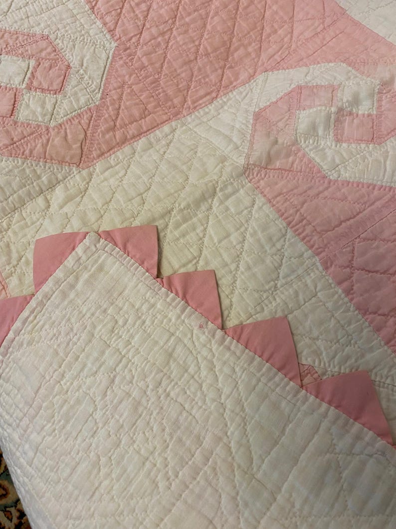 May include: A quilted textile featuring a white base with a diamond-stitched pattern and pink fabric accents. The design includes pink triangular fabric pieces attached along the edge, creating a decorative border against the white quilted surface.