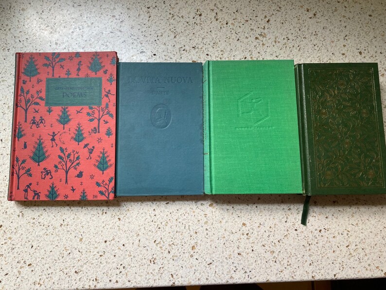 K&ouml;nnte beinhalten: Vier gebundene B&uuml;cher mit verschiedenen farbigen Einb&auml;nden. Das Buch links hat einen roten Einband mit einem Muster aus B&auml;umen und Menschen. Das Buch in der Mitte hat einen dunkelblauen Einband mit einem goldenen Design. Das Buch rechts hat einen gr&uuml;nen Einband mit einem goldenen Design.