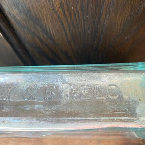 Puede incluir: Primer plano de una botella de vidrio transparente con el texto "Y & R. BELLS" grabado en la parte inferior.
