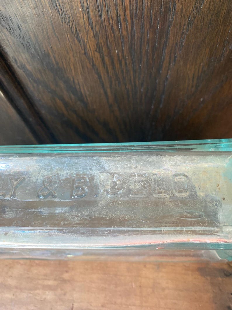 Puede incluir: Primer plano de una botella de vidrio transparente con el texto "Y & R. BELLS" grabado en la parte inferior.