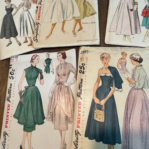 Może przedstawiać: Kolekcja czterech kopert z wykrojami krawieckimi vintage, zawierających ilustracje różnych sukienek. Koperty prezentują nazwy marek, takich jak Vogue i Simplicity, wraz z nadrukowanym tekstem zawierającym numery wzorów, ceny oraz informacje o rozmiarach.