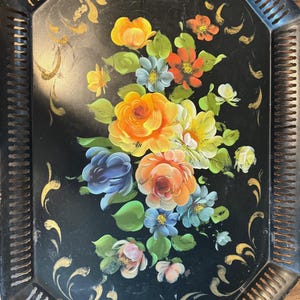 May include: Black octagonal serving tray with a floral design. The tray features a bouquet of colorful flowers in shades of yellow, orange, blue, and pink. Gold accents and cut-out handles complete the vintage look.