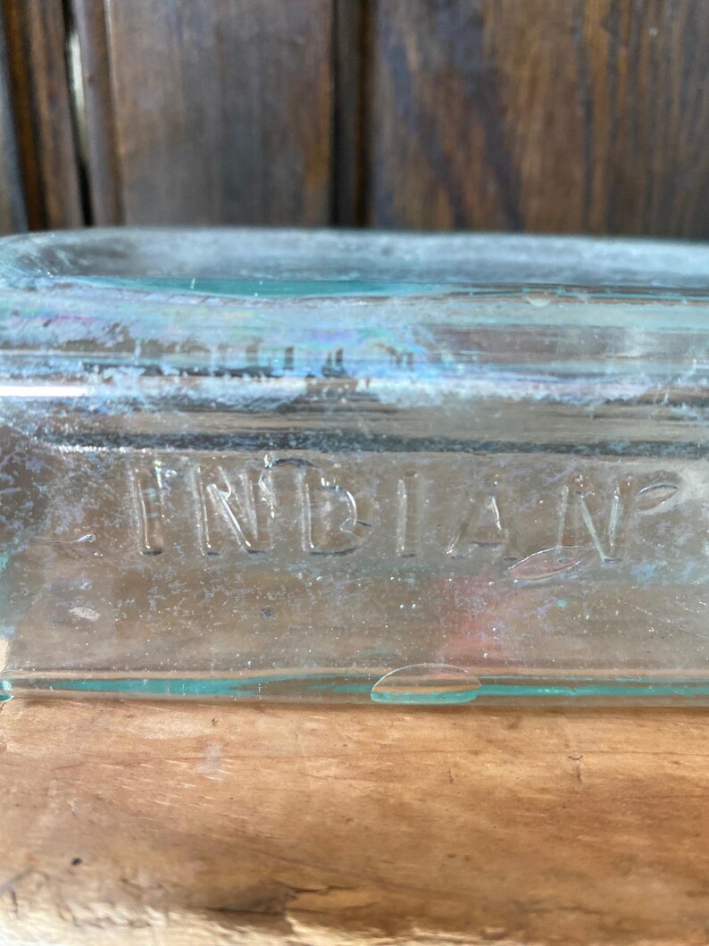 Puede incluir: Una botella de vidrio transparente con la palabra "INDIAN" grabada en el lateral.