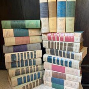 Könnte beinhalten: Eine Sammlung alter Hardcover-Bücher, die in zwei Stapeln angeordnet sind. Die Buchrücken zeigen verschiedene Farben wie Creme, Blau, Grün, Rot und Braun mit gedrucktem Text und dekorativen Details. Die Bücher wirken abgenutzt und gealtert.