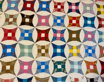 May include: A quilt with a white background and a pattern of colourful squares arranged in a circular design.