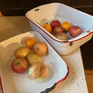 Puede incluir: Dos fuentes para hornear de esmalte blanco con bordes rojos, una llena de manzanas rojas, naranjas y cebollas, la otra con manzanas rojas, patatas y cebollas.
