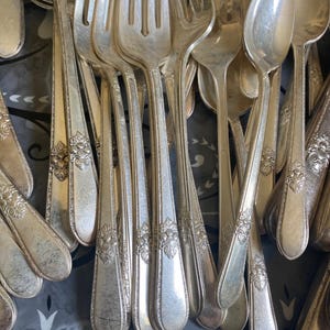 Puede incluir: Primer plano de una colección de cubiertos de plata antiguos, que incluye tenedores y cucharas. La cubertería presenta diseños florales decorativos en los mangos. Las superficies reflectantes de los tenedores y cucharas resaltan los intrincados diseños.