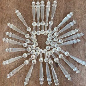 May include: A collection of clear, decorative crystal ornaments arranged in a circular pattern, resembling a starburst or snowflake. The ornaments have a faceted design and are displayed on a wooden surface.