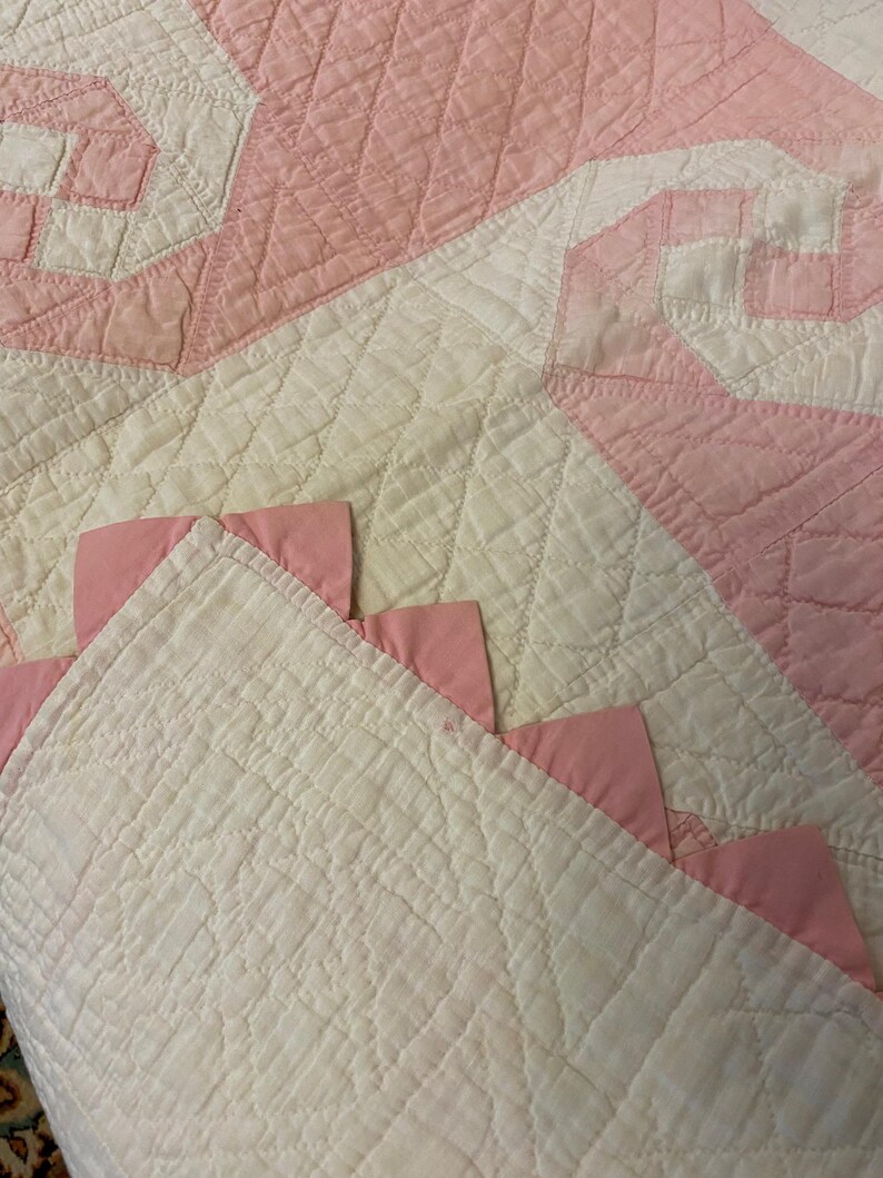 May include: A quilted textile featuring a white base with a diamond-stitched pattern and pink fabric accents. The design includes pink triangular fabric pieces attached along the edge, creating a decorative border against the white quilted surface.