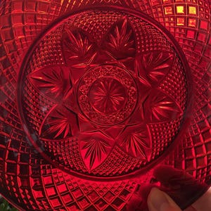 May include: A vibrant red glass plate with a detailed starburst and diamond pattern. The plate's design features a central star motif surrounded by intricate geometric shapes, creating a textured surface.