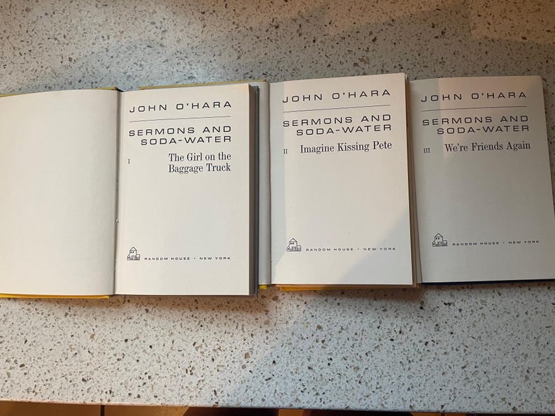 May include: Three paperback books with white covers and black text. The books are titled "Sermons and Soda-Water" by John O'Hara. The first book is volume I, "The Girl on the Baggage Truck". The second book is volume II, "Imagine Kissing Pete". The third book is volume III, "We're Friends Again".