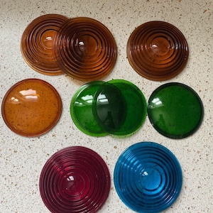 May include: Assortment of eight round, multi-colored glass lenses with a ridged pattern. The lenses are in shades of brown, green, red, and blue.