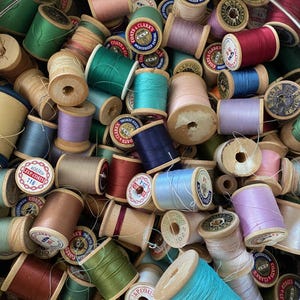 May include: A collection of spools of thread in various colours, including green, blue, pink, and red. The spools are made of wood and have labels with the text "Coats & Clarks" and "Mercerized Sewing".