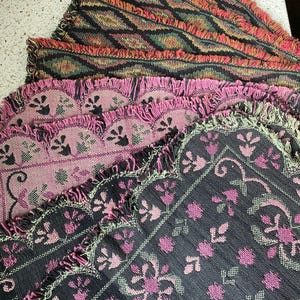 May include: A set of six woven placemats with a fringed edge. The placemats feature a variety of patterns in shades of pink, black, and green.