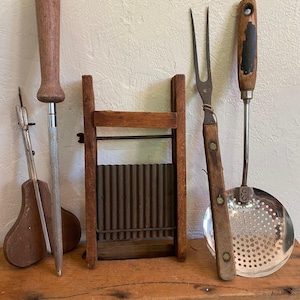 May include: A collection of vintage kitchen tools, including a wooden potato masher, a metal grater, a wooden-handled fork, and a wooden-handled metal spoon.