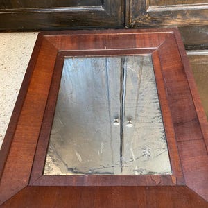 May include: A rectangular wooden frame with a mirror inside. The frame is a dark reddish brown colour. The mirror is reflecting the surrounding area.