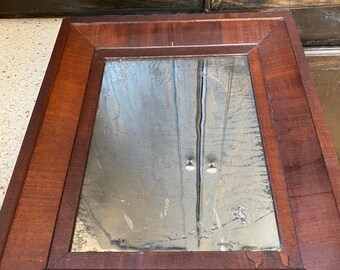 May include: A rectangular wooden frame with a mirror inside. The frame is a dark reddish brown color. The mirror is reflecting the surrounding area.