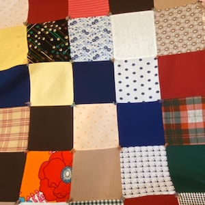 May include: A patchwork quilt composed of various fabric squares in a grid pattern. The squares feature diverse patterns and colors, including polka dots, floral prints, plaid, and solid colors like red, blue, and yellow. The quilt is a mix of textures and designs.
