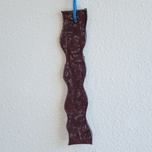 May include: A dark brown, wavy, ceramic bookmark with a blue string attached to the top.