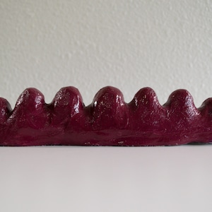 May include: A burgundy-colored, ceramic, wavy, decorative object with a smooth, glossy finish.
