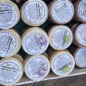 May include: A collection of eight round, white and brown soap bars with labels that read "Enjoy!" and "Osborne Ranch Soap Company, LLC." The soap bars are labelled with different scents, including "Rosemary Mint", "Lavender", and "Milk & Honey".