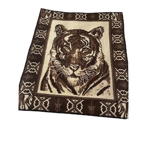 May include: A brown and cream colored throw blanket with a tiger face design. The blanket has a geometric pattern border.