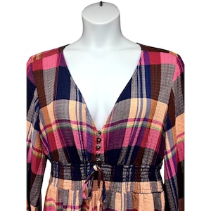 Pode incluir: Vestido xadrez multicolorido com decote em V e mangas compridas. O vestido apresenta cintura franzida e frente abotoada. O padr&atilde;o xadrez inclui tons de rosa, azul, castanho e p&ecirc;ssego.