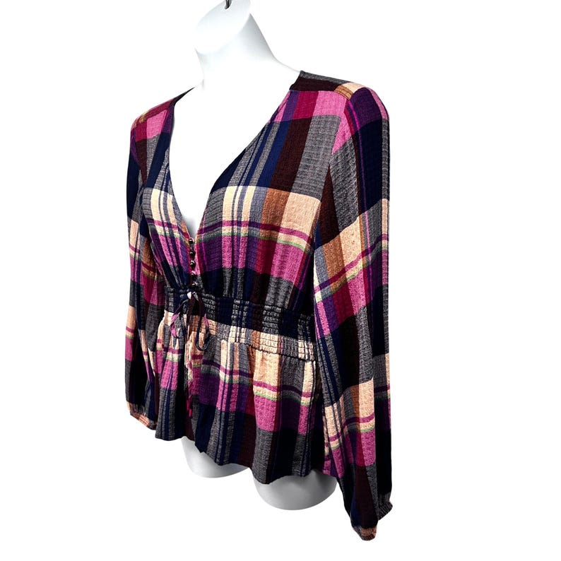 Pode incluir: Top xadrez de manga comprida em tons de rosa, roxo, azul marinho e bege. O top apresenta um decote em V profundo, uma cintura franzida e uma bainha estilo peplum. O tecido tem um aspeto macio e fluido.