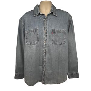 Puede incluir: Una camisa de mezclilla azul claro de manga larga con dos bolsillos en el pecho y un logotipo rojo de Levi's en el bolsillo derecho.