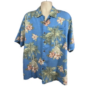 Puede incluir: Una camisa azul de manga corta con botones y estampado tropical con palmeras y flores de hibisco rosas.
