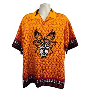 May include: A short-sleeved button-up shirt with a yellow and red flame pattern. The shirt features a black and white dragon design in the centre.