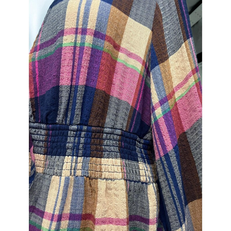 Pode incluir: Close-up de um tecido xadrez com uma mistura de cores, incluindo roxo, rosa, azul, marrom e bege. O tecido tem uma cintura franzida. O padr&atilde;o &eacute; um design xadrez cl&aacute;ssico, adequado para roupas ou decora&ccedil;&atilde;o de casa.