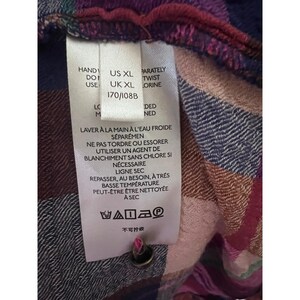 Pode incluir: Close-up de um tecido xadrez multicolorido com uma etiqueta de cuidado anexada. A etiqueta inclui instru&ccedil;&otilde;es de lavagem em franc&ecirc;s e ingl&ecirc;s, juntamente com informa&ccedil;&otilde;es de tamanho: US XL, UK XL e 170/108B.