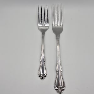 Può includere: Due forchette d'argento con manici decorati. Le forchette hanno rebbi e un motivo floreale decorativo alla base del manico. Le forchette sono in metallo lucido e riflettente, su sfondo bianco.