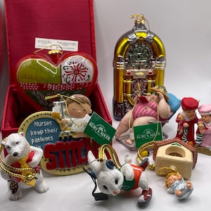 Könnte beinhalten: Eine Sammlung von Weihnachtsschmuck, darunter ein herzförmiger Schmuck mit Weihnachtsgrüßen, eine Jukebox, ein Eisbär, ein Hund mit Stethoskop und andere festliche Figuren. Die Ornamente befinden sich in einer roten Box.