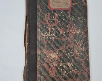 May include: A vintage notebook with a marbled cover in black and red tones. The spine is dark brown, and a small label with handwritten text is visible on the top. The edges show signs of wear, suggesting age.