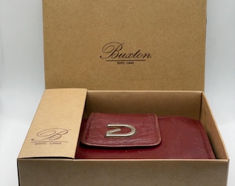May include: A red leather wallet with a silver D-shaped buckle. The wallet is in a brown cardboard box with the Buxton logo and the text "Est. 1898".