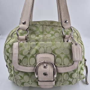 May include: A lime green and white handbag featuring a repeating C logo pattern on fabric. The bag includes white leather trim, silver-tone metal hardware, a front flap pocket with a buckle closure, and two top handles with a hanging leather tag.