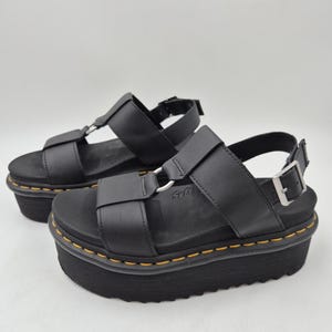 May include: Black platform sandals with adjustable straps and silver-tone hardware. The sandals have a thick, black sole with yellow stitching around the perimeter. The word "Soft" is visible on the side of the sandal.