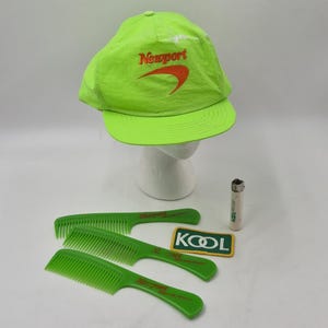 Könnte beinhalten: Eine neongrüne Baseballkappe mit orangefarbenem "Newport"-Schriftzug und einem passenden orangefarbenen Swoosh. Drei grüne Kämme und ein "Kool"-Patch sind ebenfalls sichtbar. Ein kleines Feuerzeug ist ebenfalls vorhanden.