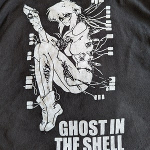 May include: Black and white graphic print of a female anime character with a gun, wires, and the text "Ghost in the Shell" on a black t-shirt.