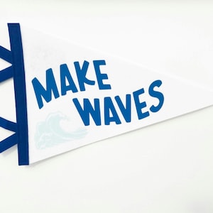 Puede incluir: Bandera de banderín blanca con texto azul "MAKE WAVES". El banderín tiene un borde azul y elementos decorativos azules. Un gráfico de olas azul claro está debajo del texto. El banderín tiene forma triangular.