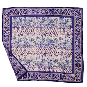 May include: A square, folded, blue and white patterned scarf. The scarf features a floral and geometric design with a dark blue border. The center has a cream background with blue floral patterns and a diamond lattice design.