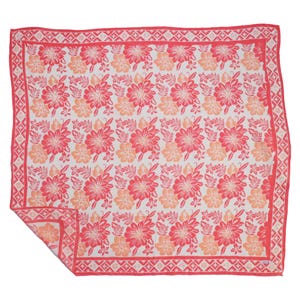 May include: A square scarf featuring a repeating floral pattern in shades of coral, pink, and white. The design includes hibiscus-like flowers and leaves, framed by a geometric diamond border in coral. One corner is folded to show the reverse side.