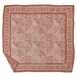 May include: A square, terracotta-colored scarf with a detailed white geometric pattern. The border features a repeating floral design. The scarf is folded at the corner, showcasing the intricate design and texture.