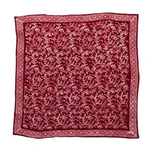 May include: A square, burgundy scarf with a repeating floral pattern in a lighter shade of red. The scarf has a decorative border and is likely made of a soft fabric. The design features detailed leaves and flowers.